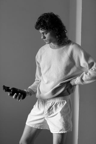 Person in a sweatshirt and boxers holding a SANDOVAL aromatic natural room spray made from gentle essential oils and perfect for use on linens and clothes.