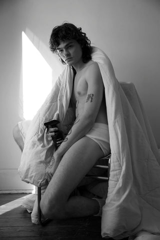 Person wrapped in a feather duvet blanket holding a bottle of WOOD, our vetiver, cedarwood, and sandalwood room and linen spray.