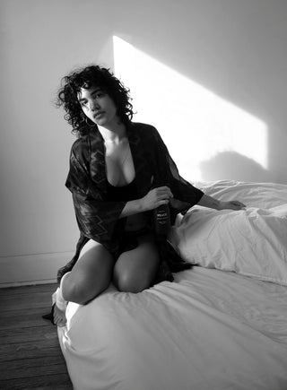 Woman in black kimono robe misting white sheets with our Peace Interior Aromatic. Use our natural aromatic sprays to refresh linens before bed or for a fragrant afternoon nap.