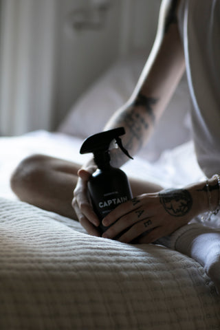 Hands holding CAPTAIN aromatic room and linen spray. Each bottle is made from natural essential oils in Los Angeles, California.